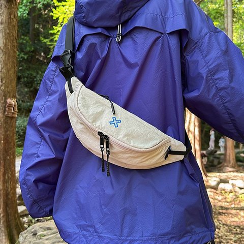Cream nylon sling bag worn across the back of a blue hooded jacket