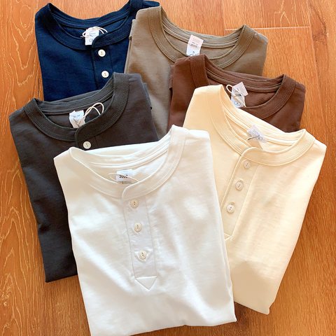 Folded Henley tees in white, cream, brown, navy and grey on a wooden floor