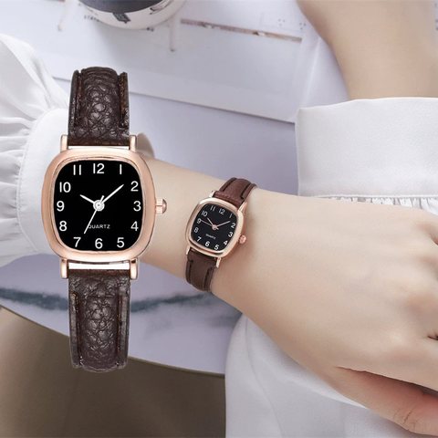 Square rose-gold quartz watch with a black dial and brown strap on a wrist